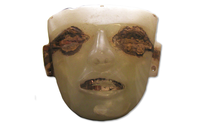 A weathered travertine face has inlaid shell teeth and iron oxide staining around the eyes, suggesting they were once inlaid with iron pyrite, or “fool’s gold.” 