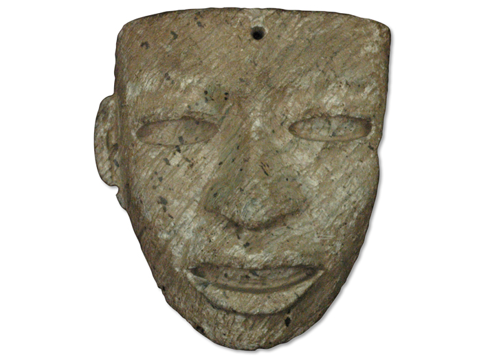 This stone face fashioned from gray-green serpentinite has a hole drilled through its temple that may have been used to attach it to a larger display. 