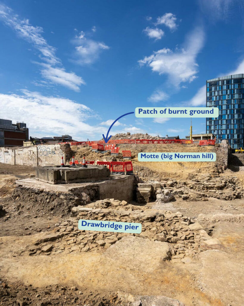 View of excavations at Sheffield Castle, England, with arrows pointing to excavated archaeological features including a burnt ground patch, motte, and drawbridge pier