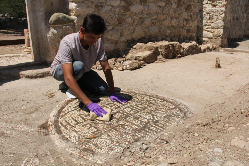 An archaeologist cleans a mosaic with a Greek inscription.