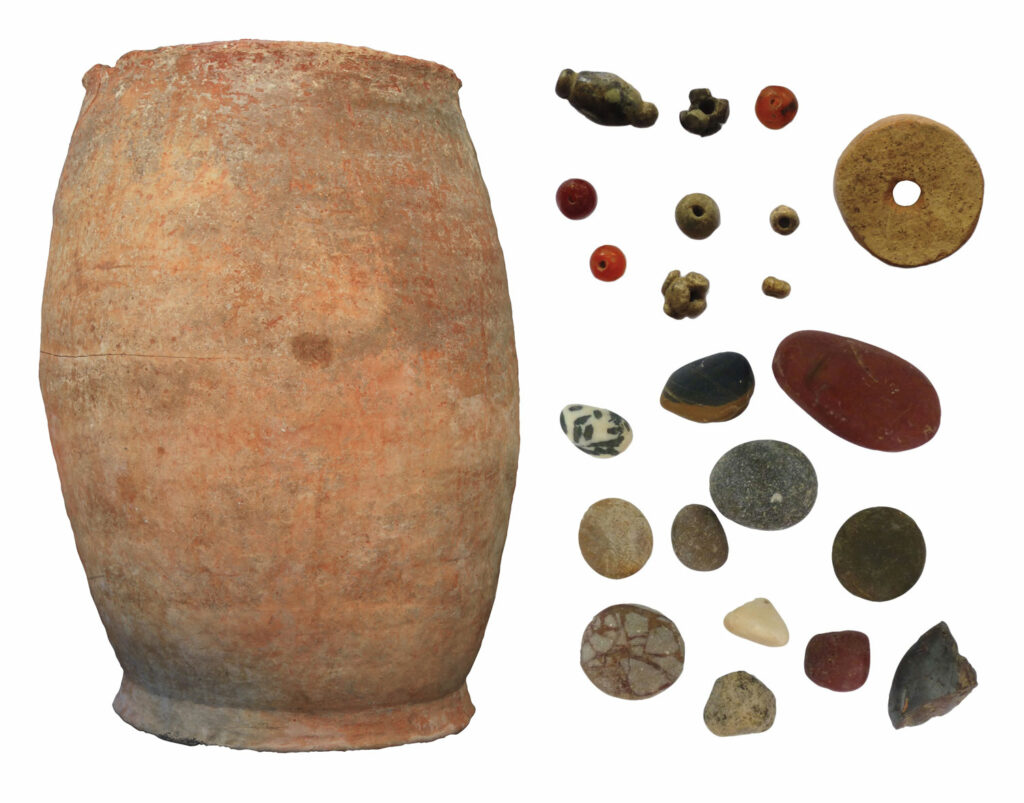 Storage jar (left) excavated at Torbulok and (clockwise from above right) a spindle whorl, pebbles, and stone and glass beads found inside the jar