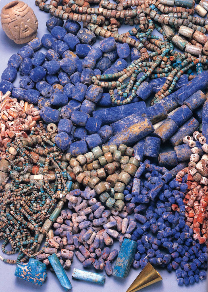 Colorful stone and shell beads, a gold earring, and a small stone vessel found in a tomb at Kuntur Wasi