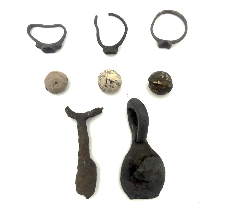 Artifacts recovered from the mission site include (top row) brass trade rings, (middle row) lead shot, and (bottom row) part of a scissor and a small copper kettle handle.
