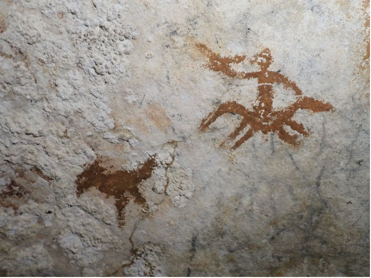 Hand stencil depicting humans and animals in a cave on the satellite island of Muna, Sulawesi, Indonesia