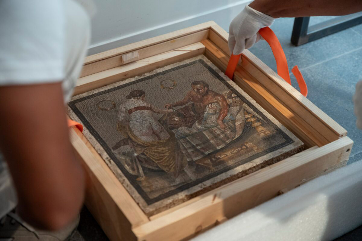 Workers lift a Roman erotic mosaic from its transport box