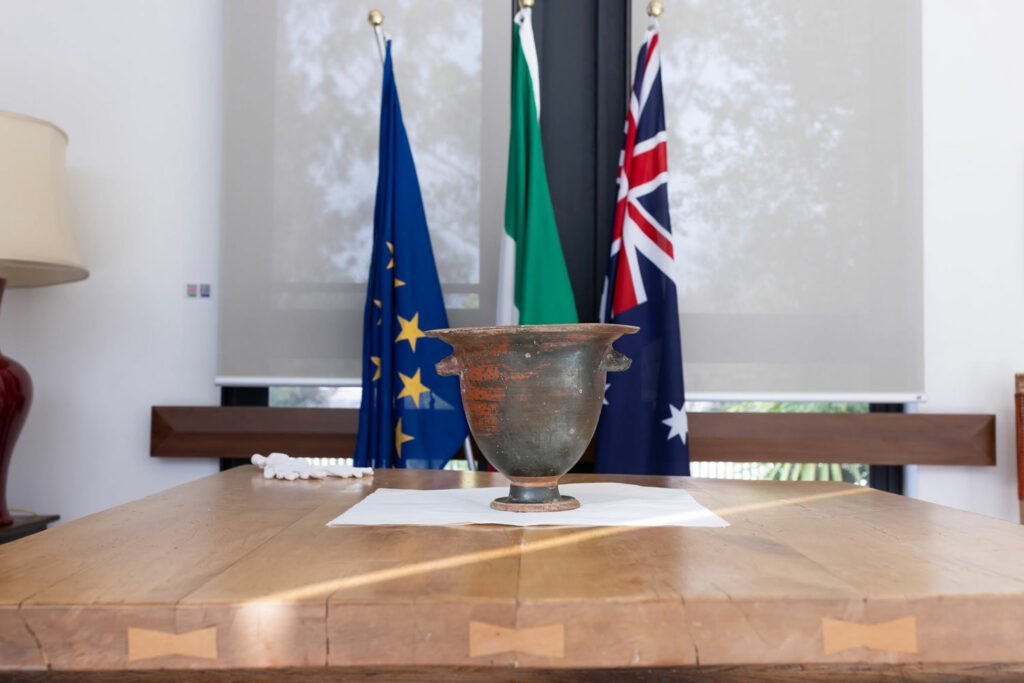 Ancient Italian bell krater sitting on a table at the Embassy of Italy in Australia, with the countries' flags in the background
