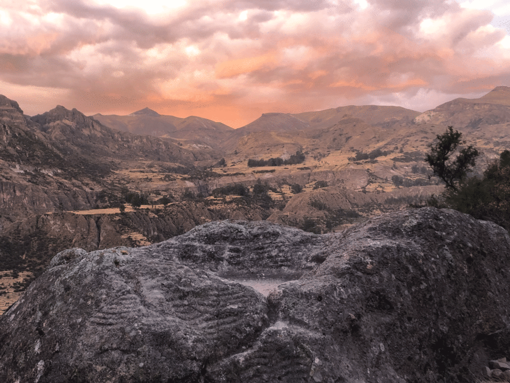 A map of agricultural terraces is carved into a large boulder overlooking a valley