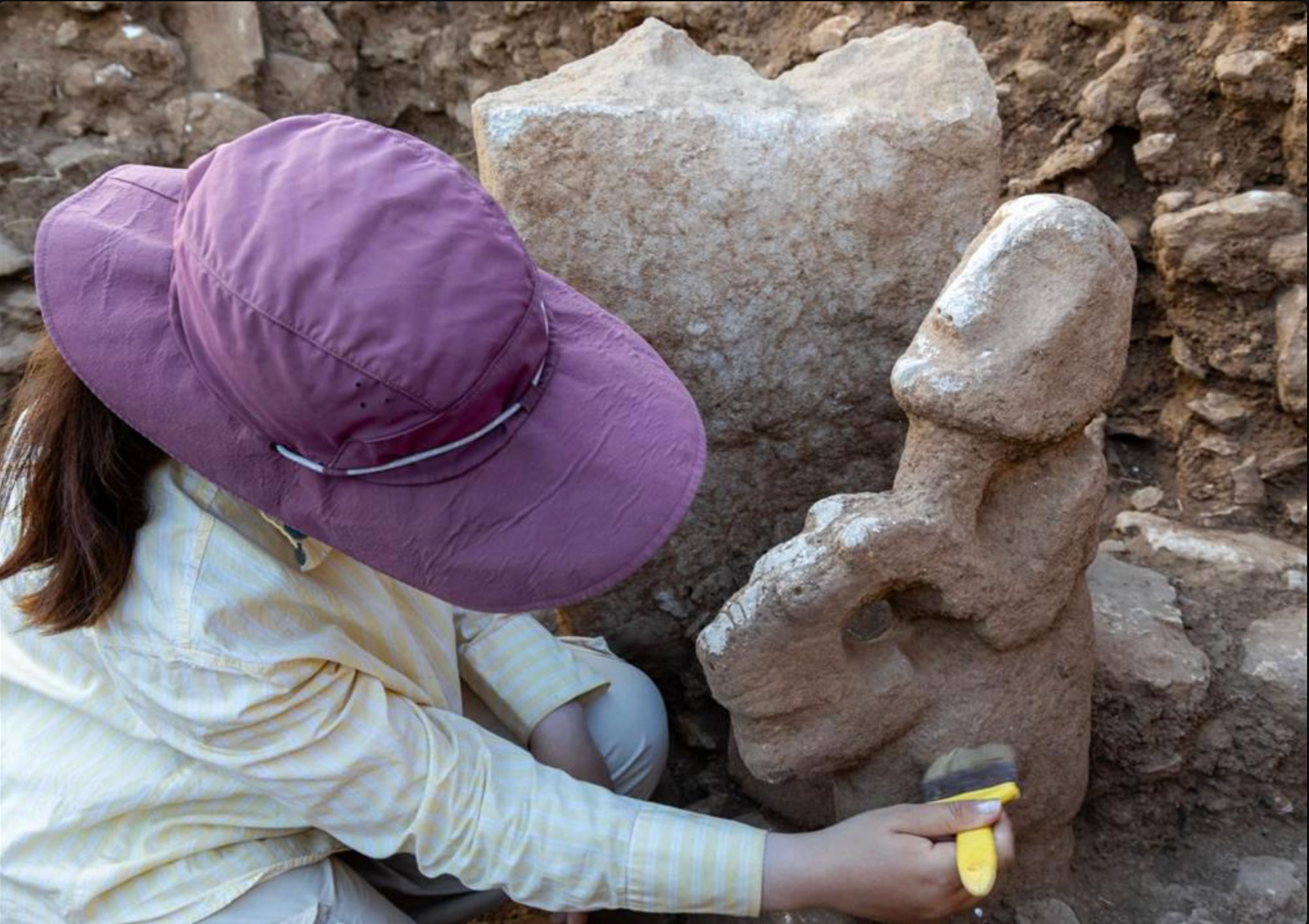 An archaeologist excavates a statue depicting a human sitting atop a leopard, Karahantepe, Turkey