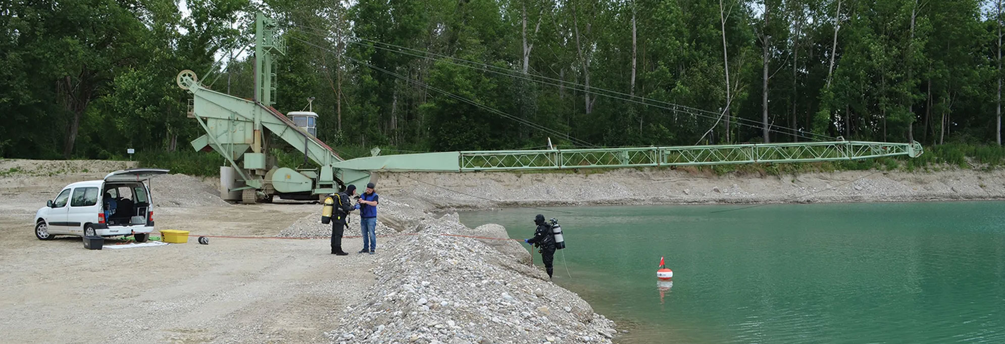 Archaeological divers investigate a gravel pit in Deinham, Austria, with the bucket excavator in the background.